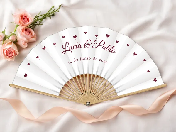 Abanico de boda personalizado “Corazones”, pequeños corazones esparcidos alrededor de los nombres Lucía & Pablo, tela color blanco e impresión en vino, sobre una mesa de boda