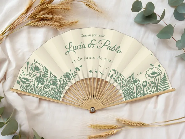 Abanico de boda personalizado “Jardín campestre”, macizo de amapolas, helechos y flores silvestres bajo los nombres Lucía & Pablo, tela color marfil e impresión en verde salvia, sobre una mesa de boda
