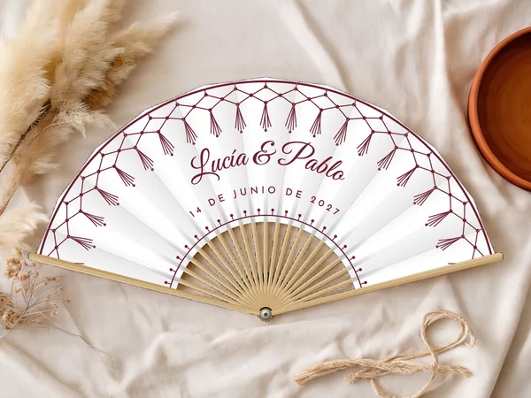 Abanico de boda personalizado “Macramé” con los nombres Lucía & Pablo, red de macramé con borlas a lo largo del borde, tela color blanco e impresión en vino, sobre una mesa de boda